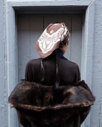 Woman wearing an oversized paisley cotton headscarf and fur stole standing in a doorway.